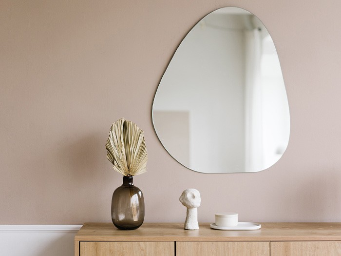 Wall featuring an oddly shaped mirror above a table.